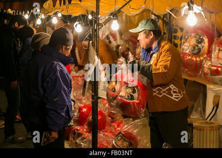 Ein Kaufmann Vertrieb Daruma Puppen außerhalb des Shorinzan-Daruma-Tempels in Stadt Takasaki, Präfektur Gunma am 6. Januar 2016, Japan. Besuchen Sie jedes Jahr Tausende von Menschen das Land berühmtesten Daruma Markt (Daruma Ichi) statt am Shorinzan Daruma Tempel am 6. Januar und 7. Takasaki Stadt ist bekannt als die Hauptstadt von Daruma Puppen und etwa 80 % der japanischen Daruma werden dort produziert. Gemäß der Tradition werden ohne Schülerinnen und Schüler auf ihre Augen gemalt Daruma Puppen verkauft. Farbe in ein Schüler bei ein Wunsch oder ein Ziel gesetzt Menschen, und wenn der Wunsch geht in Erfüllung oder das Ziel erreicht, füllen sie der Stockfoto