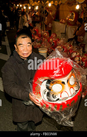 Ein Mann zeigt eine riesige Daruma-Puppe außerhalb des Shorinzan-Daruma-Tempels in Stadt Takasaki, Präfektur Gunma am 6. Januar 2016, Japan. Besuchen Sie jedes Jahr Tausende von Menschen das Land berühmtesten Daruma Markt (Daruma Ichi) statt am Shorinzan Daruma Tempel am 6. Januar und 7. Takasaki Stadt ist bekannt als die Hauptstadt von Daruma Puppen und etwa 80 % der japanischen Daruma werden dort produziert. Gemäß der Tradition werden ohne Schülerinnen und Schüler auf ihre Augen gemalt Daruma Puppen verkauft. Menschen Farbe in ein Schüler bei ein Wunsch oder ein Ziel gesetzt, und wenn der Wunsch geht in Erfüllung oder das Ziel ist erreicht, füllen sie in th Stockfoto