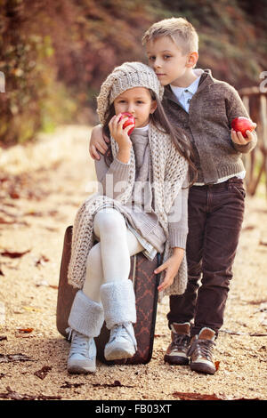 Mädchen und Jungen mit einem alten Koffer und Äpfel auf der Straße. Stockfoto