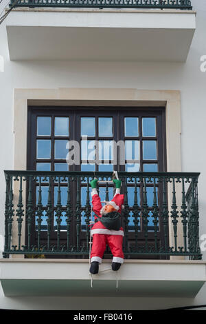 aufblasbarer Weihnachtsmann klettert einen Balkon auf einem Mehrfamilienhaus. Stockfoto