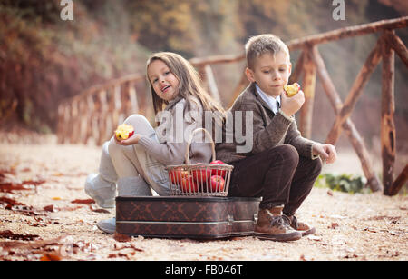 Mädchen und Jungen mit einem alten Koffer und Äpfel auf der Straße. Stockfoto