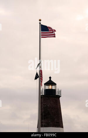 Amerikanische Flagge Wellen über Point Judith Lighthouse Tower als die Leuchte blinkt in Rhode Island in der Abenddämmerung. Stockfoto