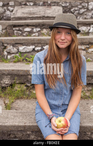 Junge hübsche Mädchen sitzen auf den steinernen Stufen mit einem Apfel in der Hand. Stockfoto