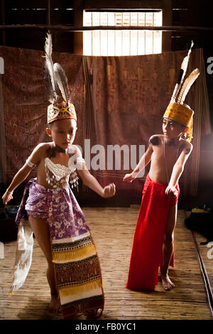 Kinder in traditionellen Trachtenanzügen, die während einer Ökotourismus-Veranstaltung im Sungai Utik Longhouse, Kapuas Hulu, West Kalimantan, Indonesien, einen Willkommenstanz vorführen. Stockfoto