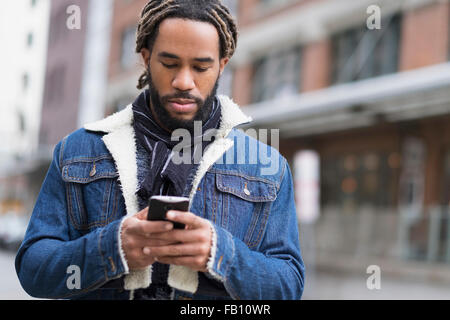 Ernster Mann mit Dreadlocks mit Smartphone in der Straße Stockfoto