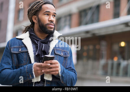 Ernster Mann mit Dreadlocks mit Smartphone in Straße Stockfoto