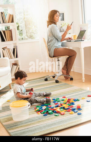 Jungen (2-3) spielt mit Spielzeug Blöcke während Mutter auf laptop Stockfoto