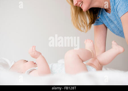 Babymädchen (12-17 Monate) auf Bett und beugte sich über Mutter liegend Stockfoto