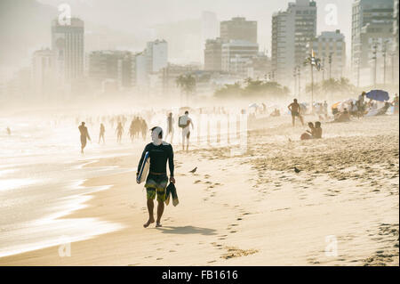 RIO DE JANEIRO, Brasilien - 18. Januar 2014: Surfer Spaziergänge am Strand von Ipanema Strand gegen eine neblige Sicht auf die Skyline. Stockfoto