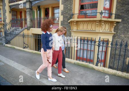 Seitenansicht von Freunden zu Fuß hinunter Wohn-Straße Arm in Arm lächelnd, Shoreditch, London Stockfoto
