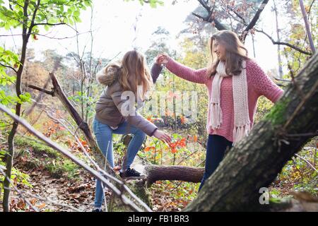 Junges Mädchen im Wald hilft Freund auf umgestürzten Baumstamm lächelnd Klettern Stockfoto
