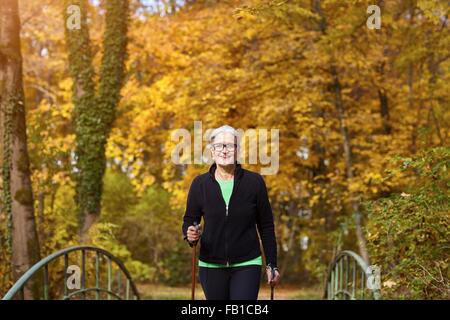 Ältere weibliche nordic Walker Kreuzung Fußgängerbrücke im Herbst park Stockfoto