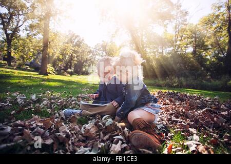 Kinder sitzen auf Herbst Blatt bedeckt Rasen blickte mit digital-Tablette Stockfoto