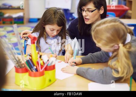 Mädchen und Lehrer zeichnen am Schreibtisch im Klassenzimmer der Grundschule Stockfoto