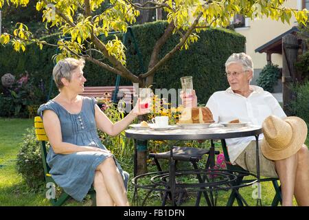 Älteres Paar, am Tisch im Garten sitzen, trinken Stockfoto