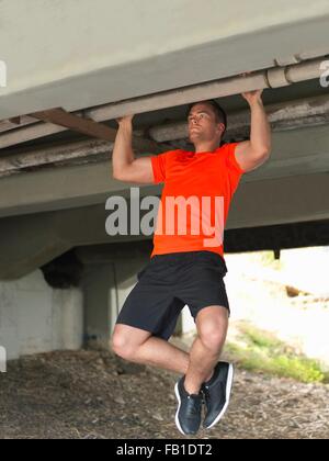 Junger Mann tun Pull ups unter Brücke Stockfoto