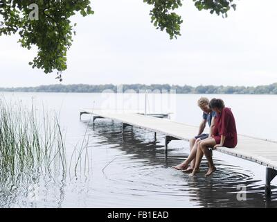 Paar sitzt am Pier nebeneinander DIP Zehen im Wasser, Kopenhagen, Dänemark Stockfoto