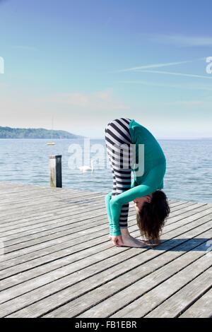 Seitenansicht des Reife Frau am Pier von Ocean holding Knöchel bücken Stockfoto