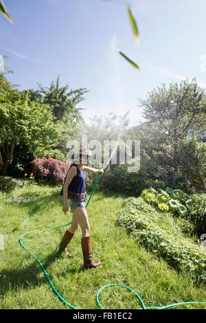 Seitenansicht des Reife Frau im Garten Spritzen Wasser in Luft mit Schlauch Stockfoto