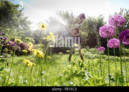 Blick durch Blumen Reife Frau im Garten Bewässerung Blumen mit Schlauch Stockfoto