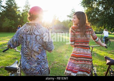 Rückansicht des Partygoing paar Ankunft auf Fahrrädern zu sunset Park party Stockfoto