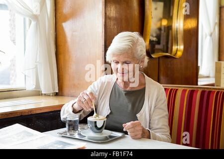 Ältere Frau sitzen im Café, Kaffee rühren Stockfoto