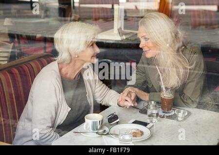 Mutter und Tochter beisammen sitzen im Café, Hand in Hand, durch Café Fenster gesehen Stockfoto