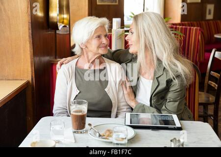 Mutter und Tochter beisammen sitzen im Café, Tochter Arm um Mutter, digital-Tablette auf Tisch Stockfoto