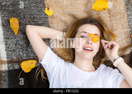 Junge Frau auf der Decke liegend, die Auge mit Blatt Stockfoto