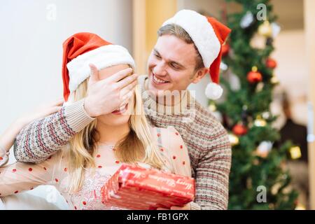 Junger Mann Freundinnen Augen bedecken, während Übergabe Weihnachtsgeschenk Stockfoto