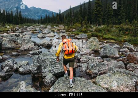 Rückansicht des Mitte erwachsener Mann mit Rucksack zu Fuß auf felsigen Flussbett, Moraine Lake, Banff Nationalpark, Alberta Kanada Stockfoto