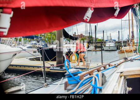 Junge Frau auf Marina Pier festmachen Segelboot Blick auf die Kamera zu Lächeln Stockfoto