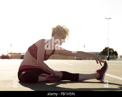 Junge Frau, die ihre Zehen zu berühren, beim training auf Parkplatz Stockfoto