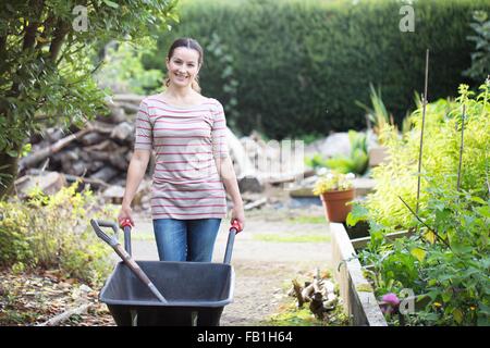 Porträt von weiblichen Gärtner drängen Schubkarre in rustikalen Bio-Garten Stockfoto