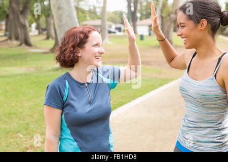 Junge Frauen tragen Sportbekleidung von Angesicht zu Angesicht lächelnd dabei hohe fünf Stockfoto