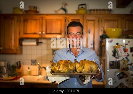 Porträt von reifer Mann hält Grillhähnchen in Küche Stockfoto