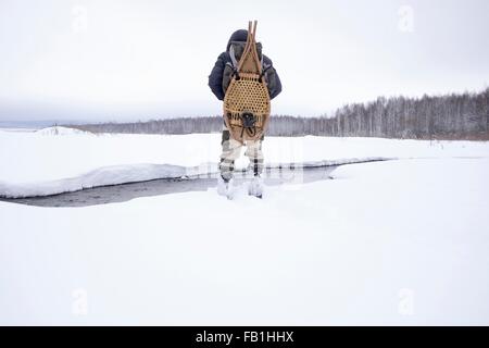 Rückansicht des Mitte erwachsenen Mannes in schneebedeckten Feld Fluss tragen traditionelle Schneeschuhe, Ural, Russland Stockfoto