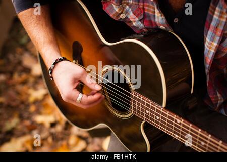 Schuss der junge Mann spielt Gitarre im herbstlichen Wald beschnitten Stockfoto