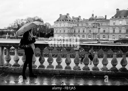 Ein schönes junges Mädchen genießt die Aussicht unter einem Dach an einem regnerischen Tag im Jardin du Luxembourg in Paris, Frankreich. Stockfoto