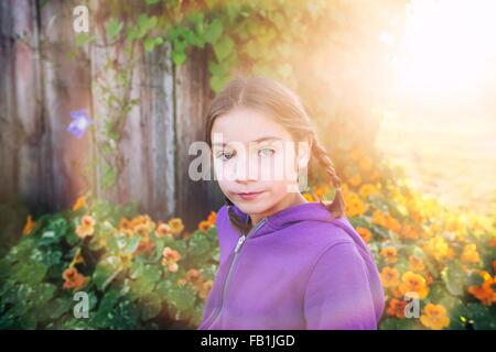 Porträt von Mädchen mit Zöpfen vor orange Blumen Blick in die Kamera Stockfoto