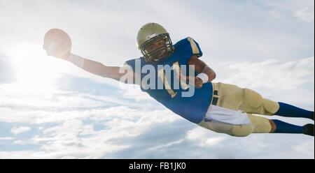 Männliche Teenager American Footballspieler Ball Mitte Luft gegen sonnigen Himmel fängt Stockfoto