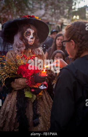 Kostümiert mit einem Skelett Gesicht, La Calavera Catrina ("Dapper Skelett") Leuchten Kerzen am Denkmal Altäre während der Tag der Toten oder Dia de Muertos Zeremonien unter Hispanics in Santa Ana, Kalifornien. Der Urlaub konzentriert sich auf Versammlungen von Familie und Freunden zu beten Stockfoto