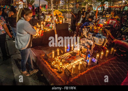 Von votive Kerzen beleuchtet, ein Altar zu Ehren eines verstorbenen Familienmitglieds am mexikanischen Tag der Toten oder Dia des Muertos in einem hispanischen Viertel in Santa Ana, CA. Hinweis gerahmtes Porträt im Vordergrund links ausgestellt und Bestattung Kreuz im Zentrum. Die h Stockfoto