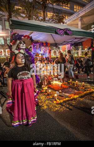 Ein Altar zu Ehren eines verstorbenen Familienmitglieds ist ausgestellt am mexikanischen Tag der Toten oder Dia des Muertos in einem hispanischen Viertel in Santa Ana, CA. Hinweis gestaltet Porträt des verstorbenen im Hintergrund, Mutter und Tochter von votive Kerzen beleuchtet, ich Stockfoto