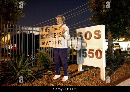 Eine leitende ehrenamtliche Frau hält ein hausgemachten Schild vor einem Obdachlosenheim in Costa Mesa, CA, hundertprozentige Verpflichtung des Unternehmens zum Ausdruck zu bringen. Stockfoto