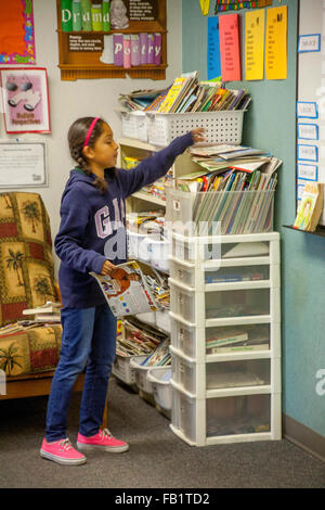 Eine Hispanic dritte Klasse Mädchen wählt Lesestoff aus einem Klassenzimmer Buch Ecken in San Clemente, CA. Hinweis literarische Plakate. Stockfoto