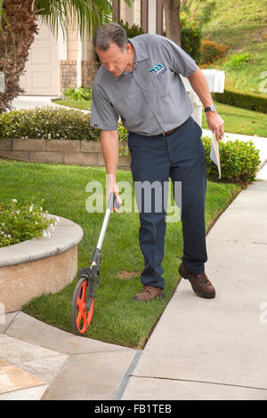 Mit den Plänen zu installieren Kunstrasen während einer Dürre prüft ein Wasser-Dienstprogramme-Supervisor der Rasenfläche eines Hauses in Laguna Niguel, CA. Hinweis Messrad. Stockfoto