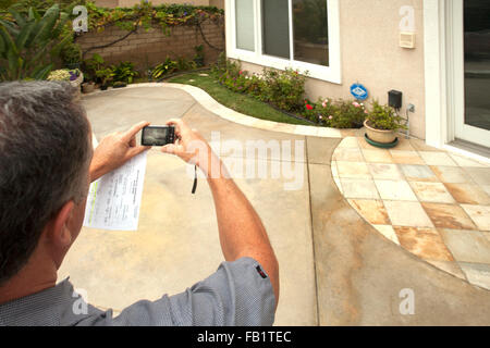 Mit den Plänen zu installieren Kunstrasen während einer Dürre prüft ein Wasser-Dienstprogramme-Supervisor die Rasenfläche auf den Hinterhof eines Hauses in Laguna Niguel, CA. beachten Sie Handy-Kamera. Stockfoto