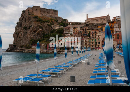 Blauer Sonnenschirm und Liegestuhl am Strand vor italienischen Kleinstadt auf Klippe unter blauem Himmel Stockfoto