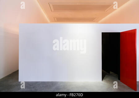 Fokus auf große weiße Wand und rote geöffnete Tür mit Dunkelheit im Inneren in einer großen Halle Stockfoto